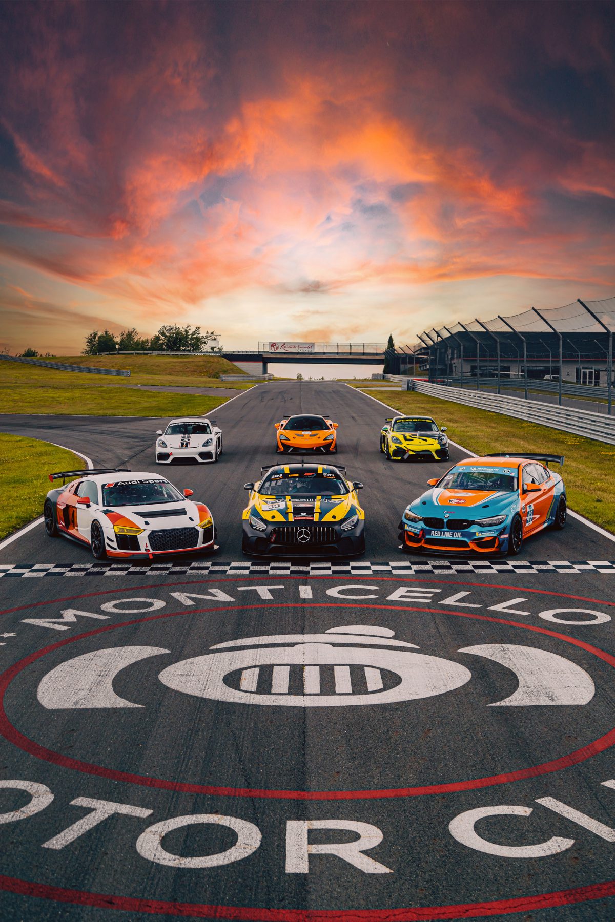 a group of race cars are parked on the start/finish line during sunset