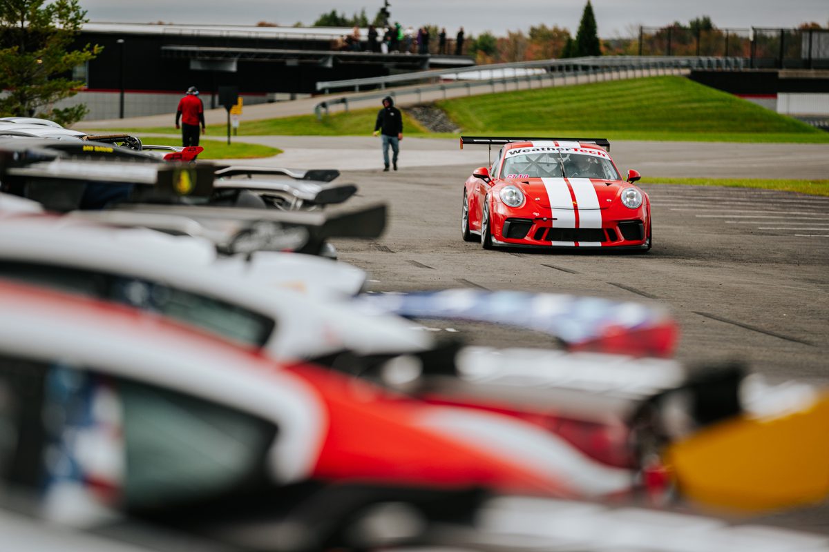 A red and white Porsche race car driving down the grid near parked race cars