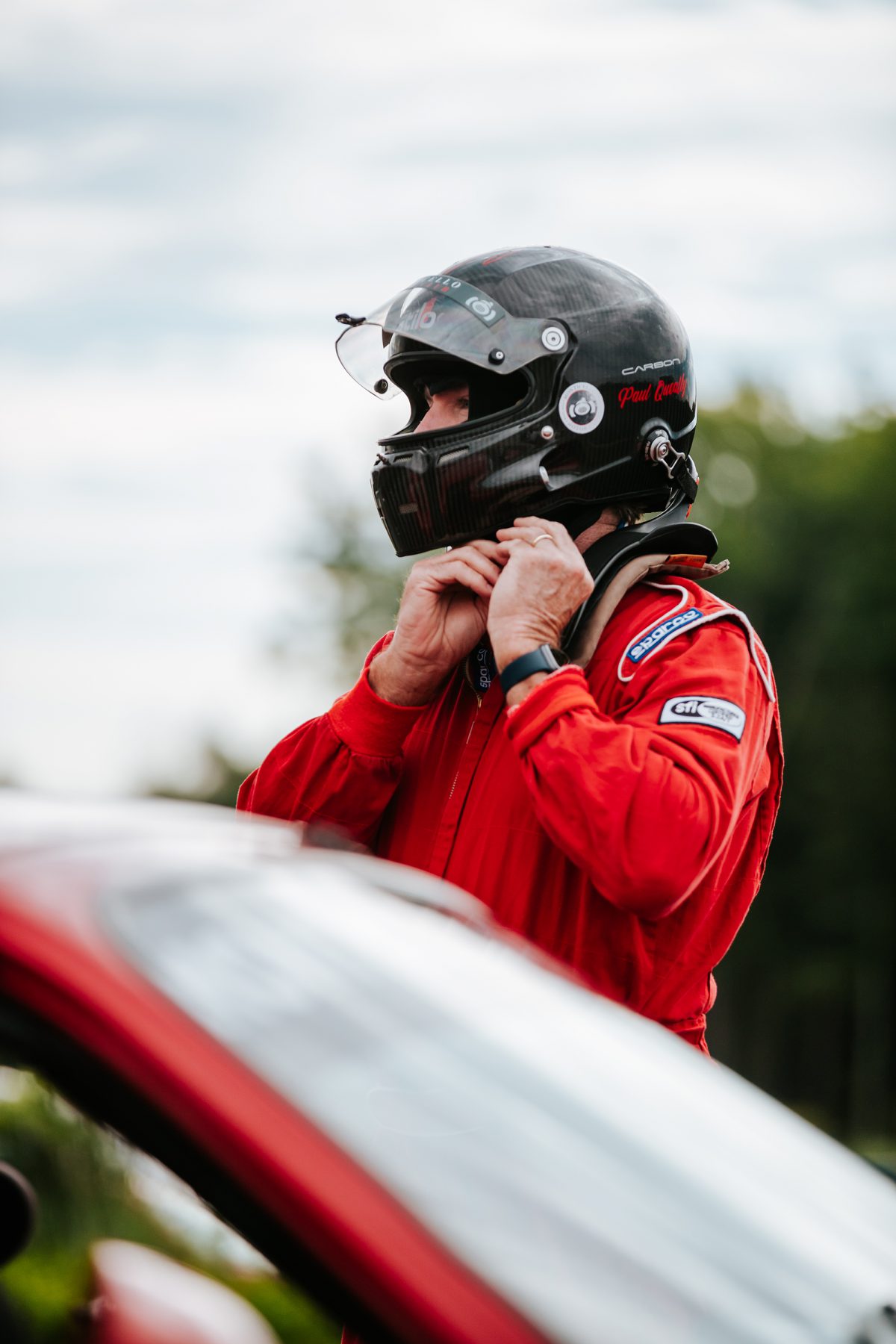 A driver in a race suit is securing his helmet