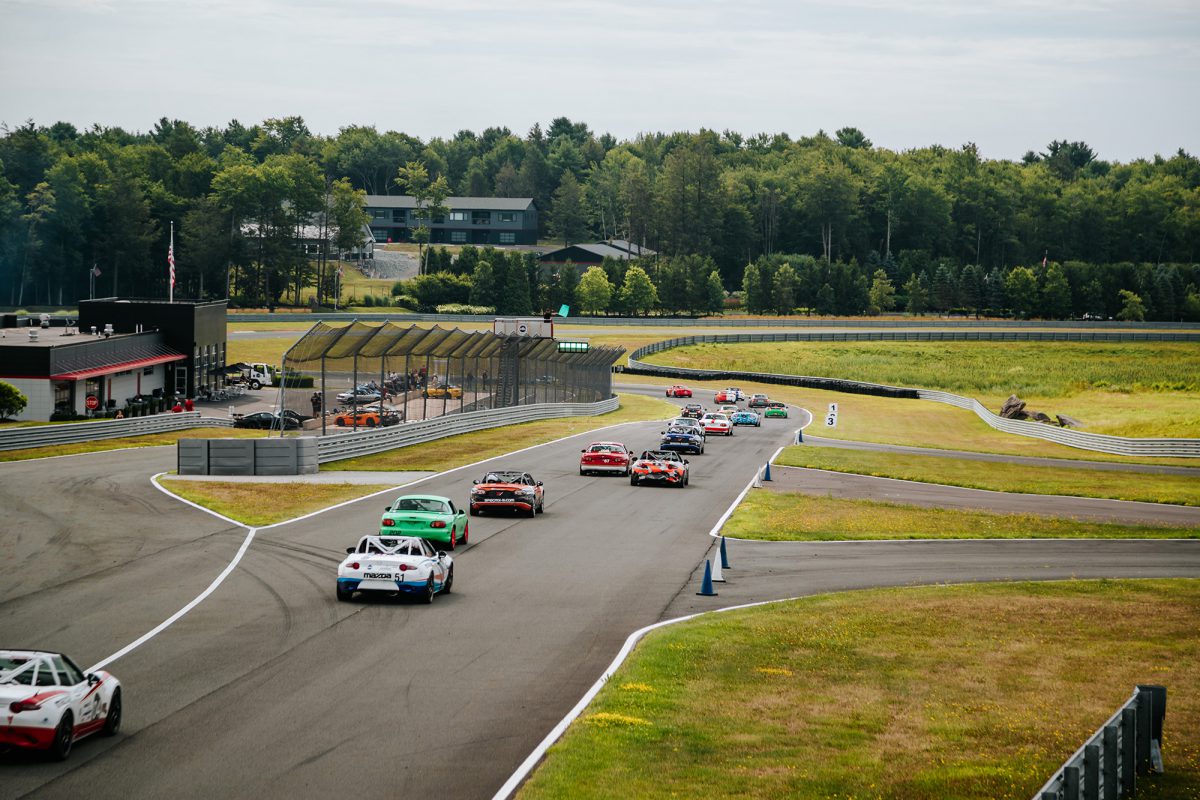 A group of Mazda Miatas are racing down the straight away as the green flag drops