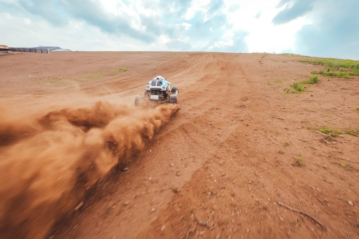 a silver cross kart racing through the dirt, with a cloud of dust behind it