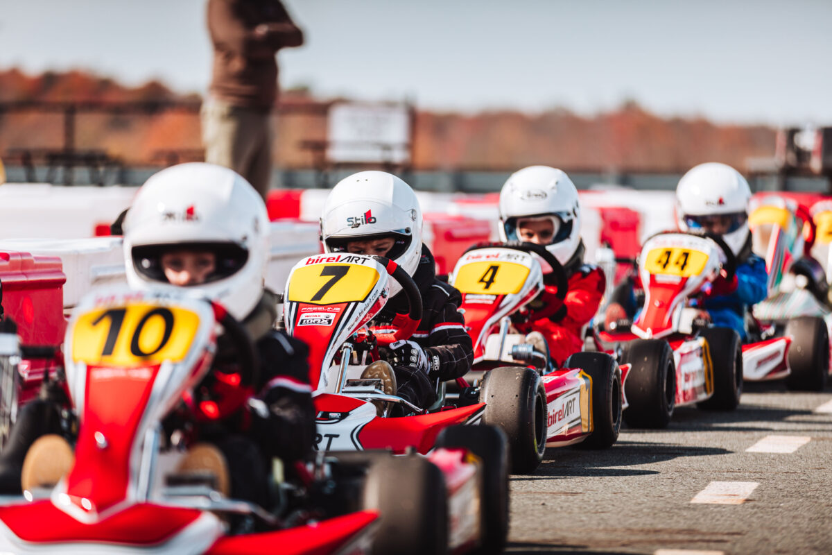 A group of children sit in go karts with helmets on as they wait to go on the go kart track