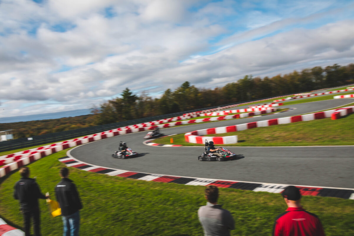 Go Karts are racing down the track as people are spectating in the foreground