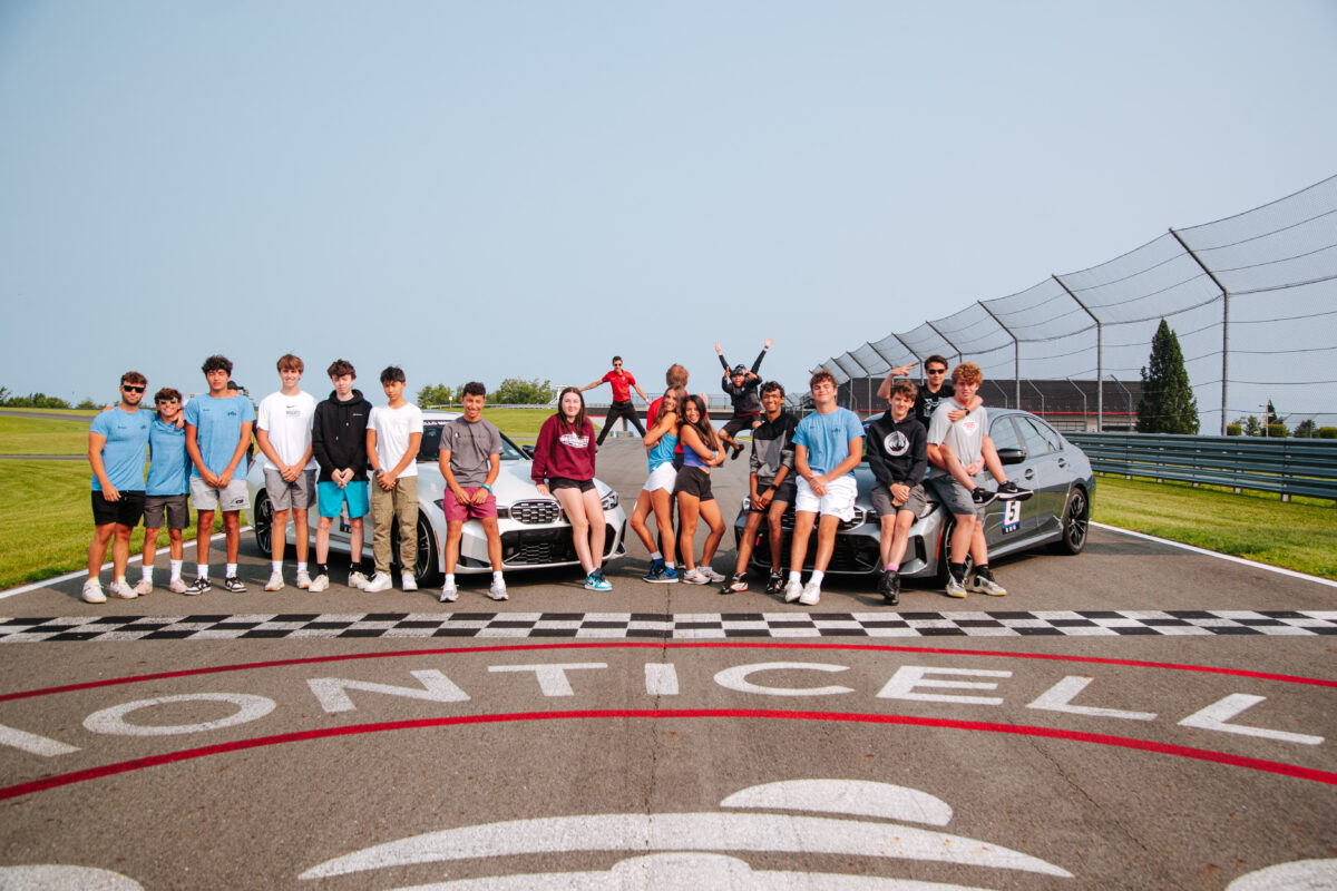 a group of teenagers are posing in front of two bmws on the start/finish line
