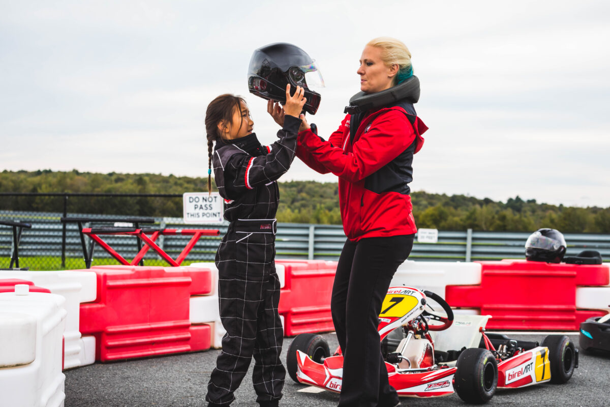 A female instructor helps a young female with her helmet at the Karting Track