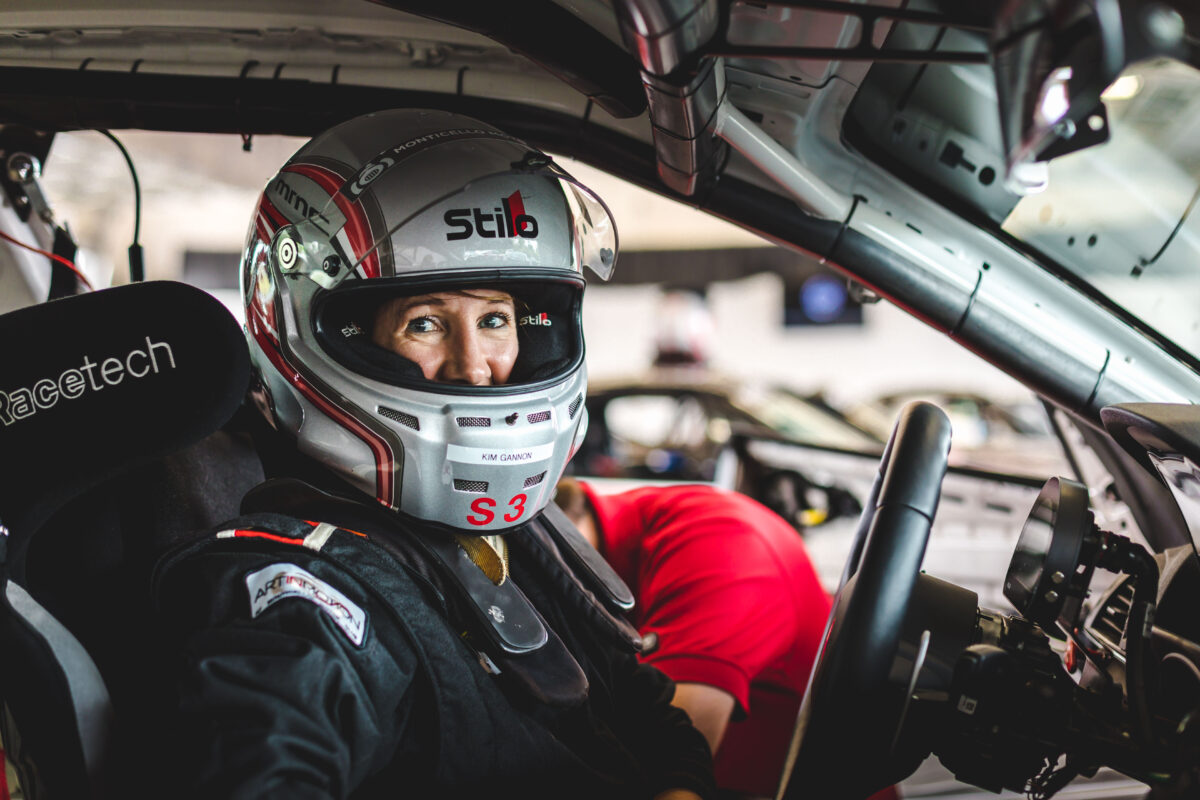 a woman with a helmet on looks at the camera as she is sitting in a race car