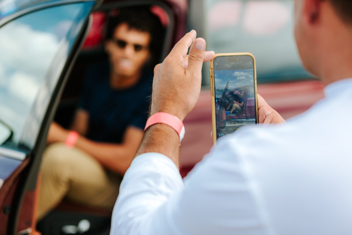 A man is sitting in a car getting his picture taken with a camera phone